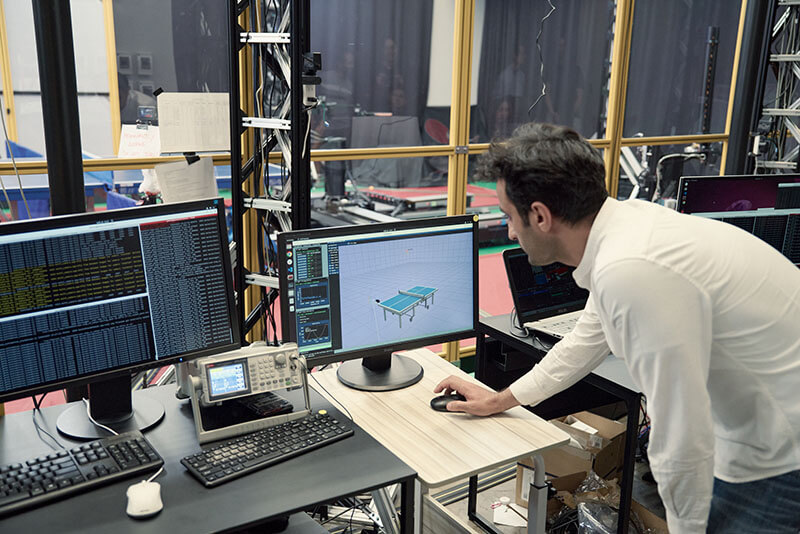 A man uses a computer to train an autonomous robot how to play table tennis.